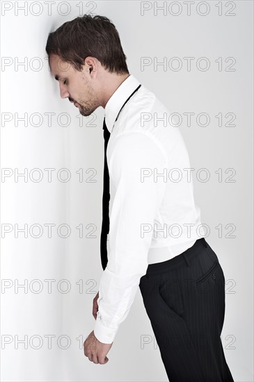 Desperate young man wearing a shirt and a tie standing with his head leaning against a wall