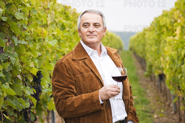 Winemaker or vintner standing with a glass of red wine in his vineyard