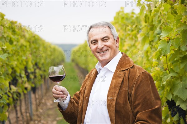 Winemaker or vintner standing with a glass of red wine in his vineyard