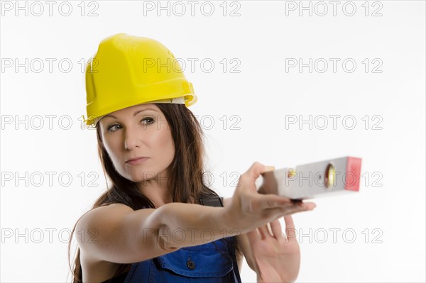 Woman wearing blue overalls and a hardhat holding a spirit level