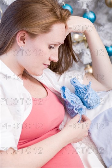 Pregnant woman with baby shoes sitting in front of a Christmas tree