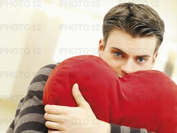 Young man holding a heart-shaped pillow