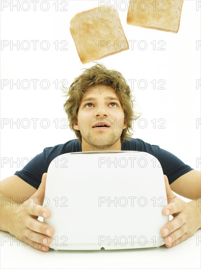 Young man looking at slices of toast as they pop out of a toaster