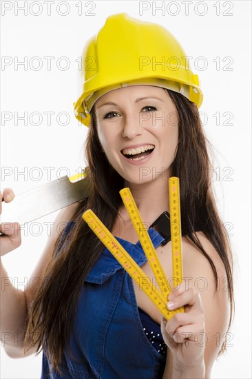 Woman wearing blue overalls and a hardhat holding a folding carpenter's ruler and a spirit level