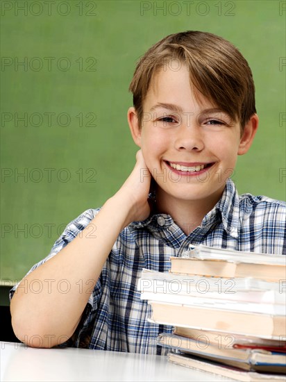 Schoolboy in front of a school blackboard with a stack of books