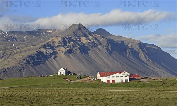 Farm and mountain scenery with eroded scree slope in the evening light near Hofn