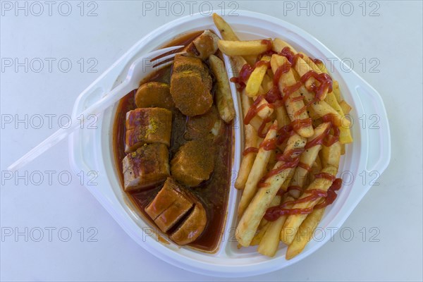 Currywurst with French fries with plastic fork on a plastic plate