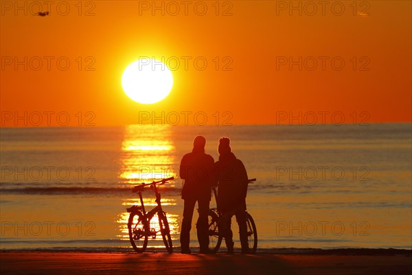Couples with bikes on the beach watching the sunset