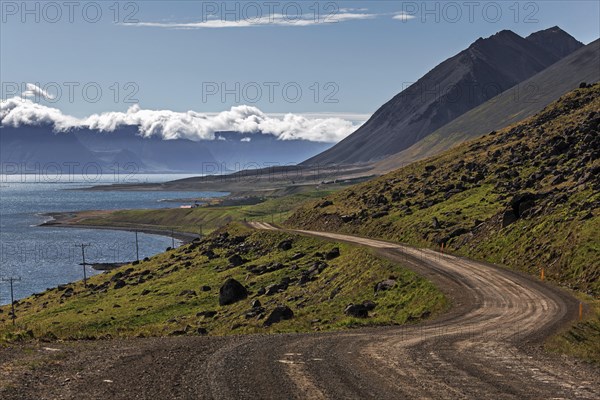 Gravel road meanders along a fjord through volcanic landscape