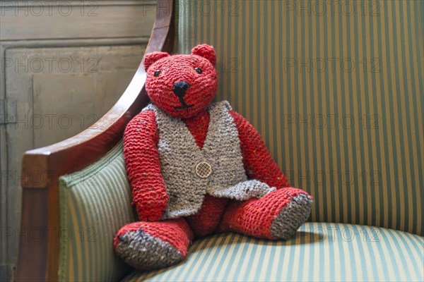 Knitted red teddy bear with vest on striped armchair