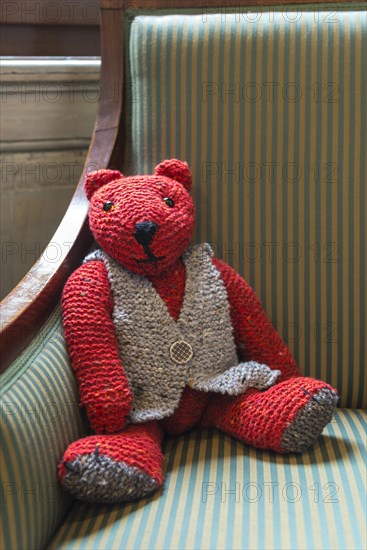 Knitted red teddy bear with vest on striped armchair