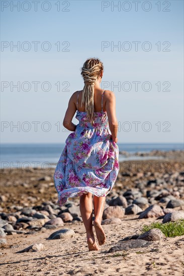 woman with dreadlocks walks barefoot in the sand at the coast