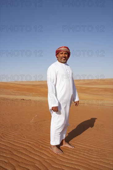 Bedouin in traditional dress stands in the sandy desert
