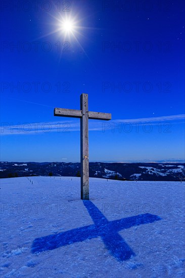 Summit cross in snow with starry sky by moonlight