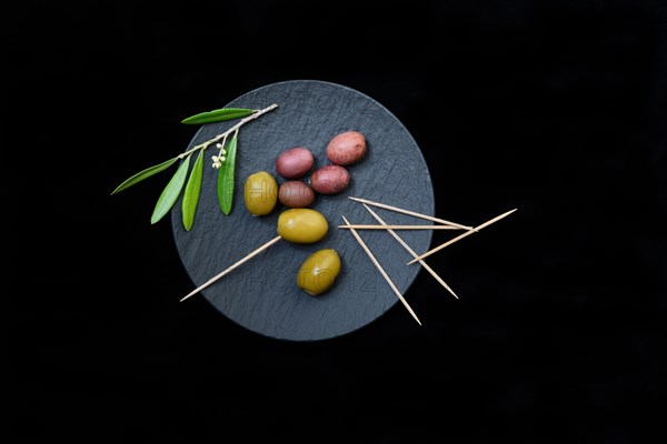 Green and black olives with toothpick on black plate