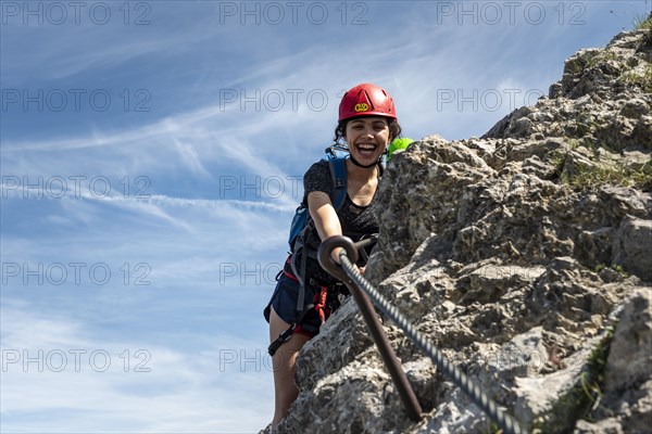 Laughing young woman with climbing helmet and on rock secured with rope