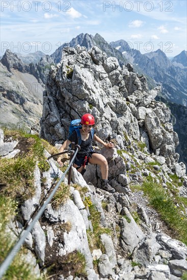 Laughing young woman with climbing helmet on secured rock