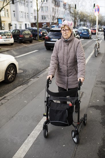 Senior citizen with rollator crosses a street in the city