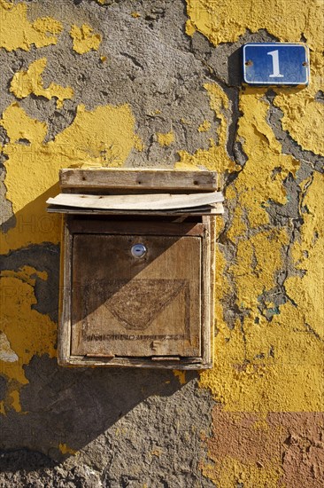 Wooden mailbox with house number one on house wall with flaking paint