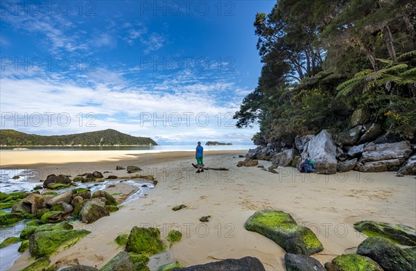 Young woman standing on beach with moss-covered rocks