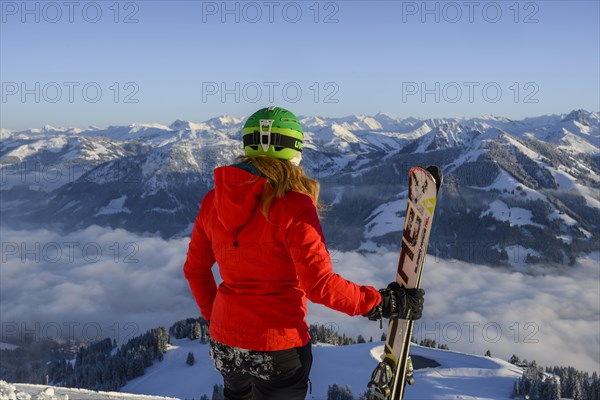 Skier with ski helmet and ski looks at mountain panorama
