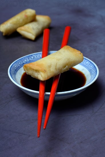 Spring roll on chopsticks and bowl with soy sauce