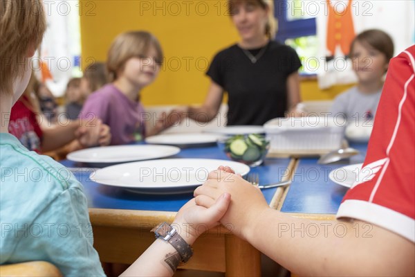 Children and nursery school teacher in the dining room of the kindergarten hold hands and speak a table motto
