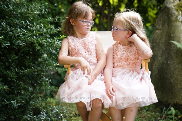 Portrait of two sisters sitting together on a garden chair (6 years old