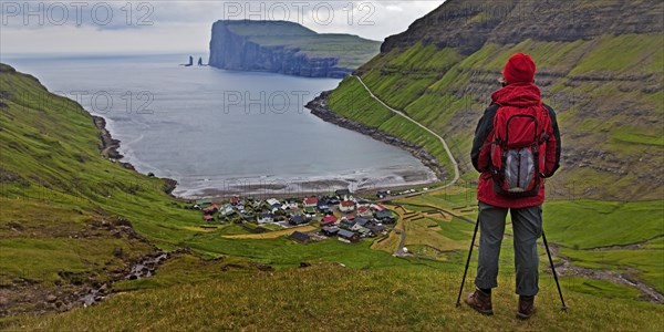 A hiker looks at the small village Tjornuvik and the Atlantic Ocean