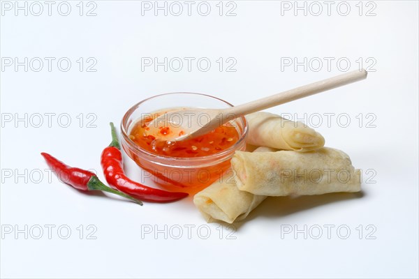 Chilli sauce in small bowls with chilli peppers and mini spring rolls