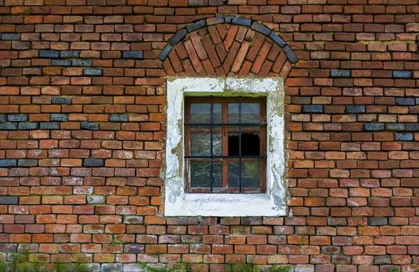 Wall of red bricks with barred stable window and broken panes