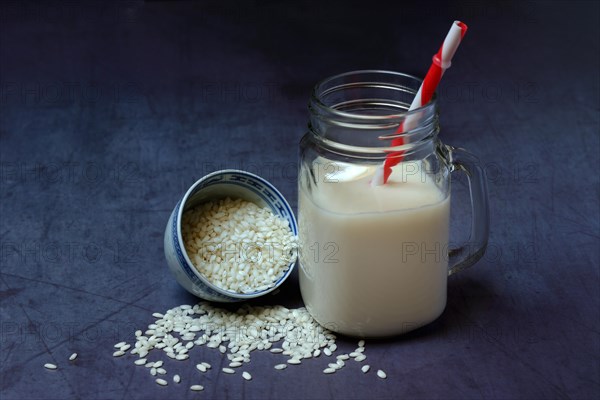 Rice milk in glass with drinking straw and rice grains