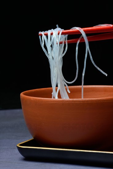 Asian glass noodles on chopsticks over bowl