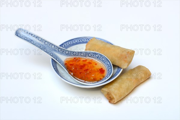 Chilli sauce in Asian spoon and mini spring rolls