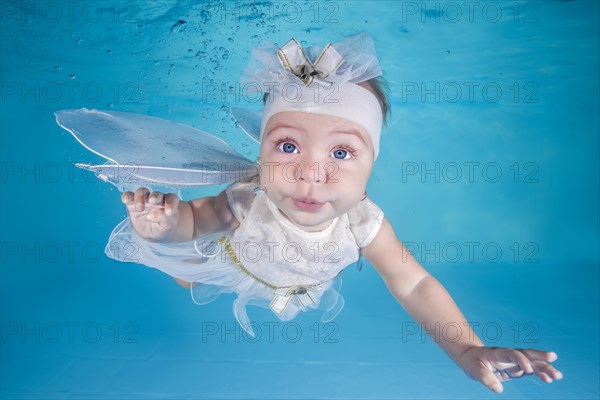 Little girl in fairy costume dives underwater in a swimming pool