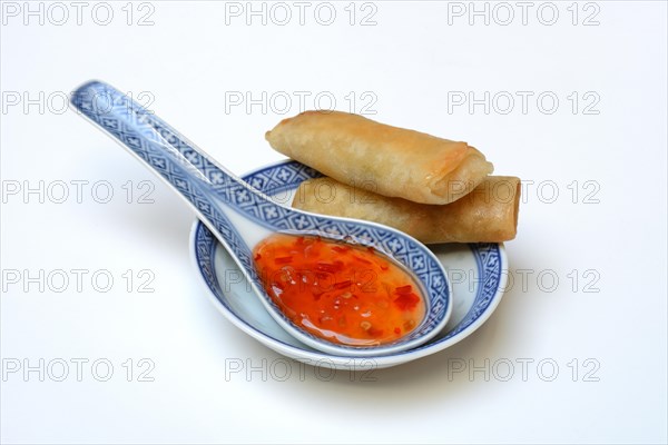 Chilli sauce in Asian spoon and mini spring rolls