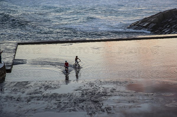 Two children ride their bikes on flooded terrace