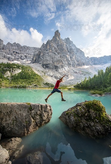 Hiker jumps from stone to stone at the turquoise-green Sorapis lake