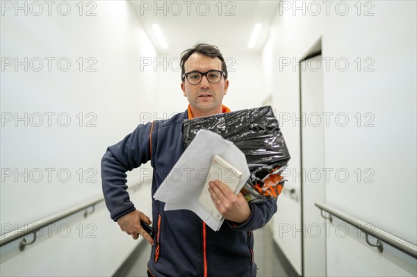 Courier with the package and documents in his hand in white corridor
