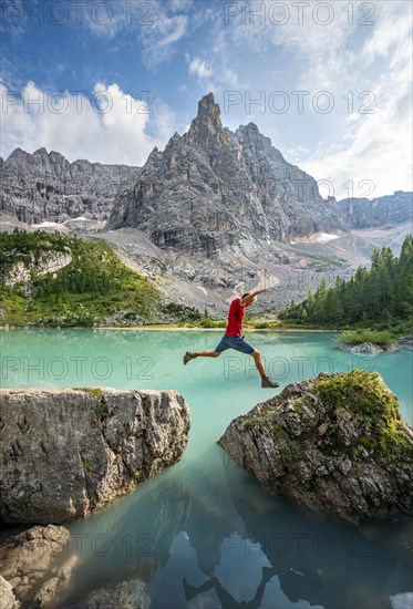 Hiker jumps from stone to stone at the turquoise green Sorapis lake