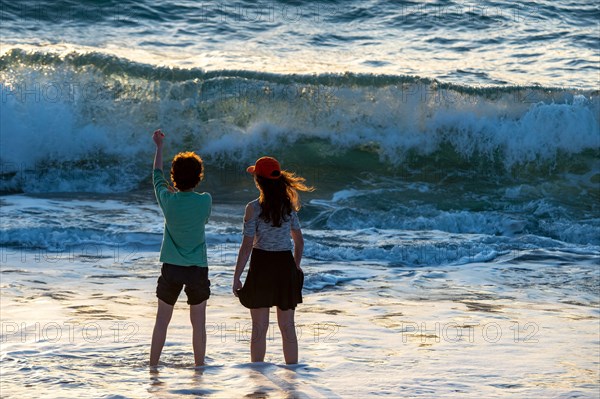 A little girl and a boy in front of the waves by the sea