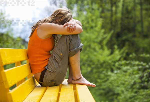 Young woman sitting sad and huddled on a bench