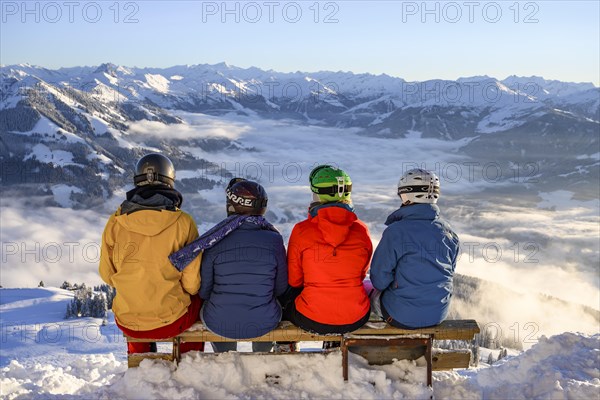 Skiers sitting on a bench and looking down on snow-covered mountains