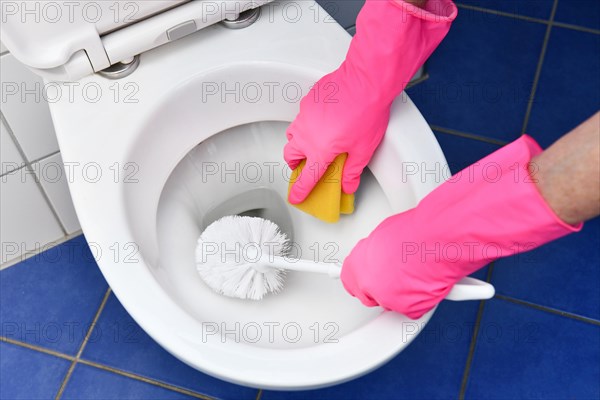 Person with rubber gloves cleans toilet with brush