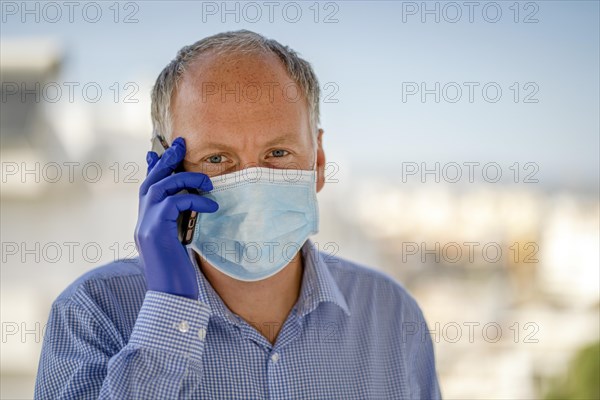 Man using protective mask and blue latex gloves while using mobile phone