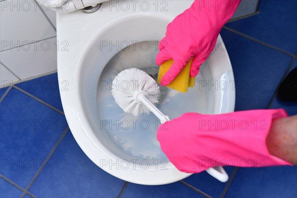 Person with rubber gloves cleans toilet with brush