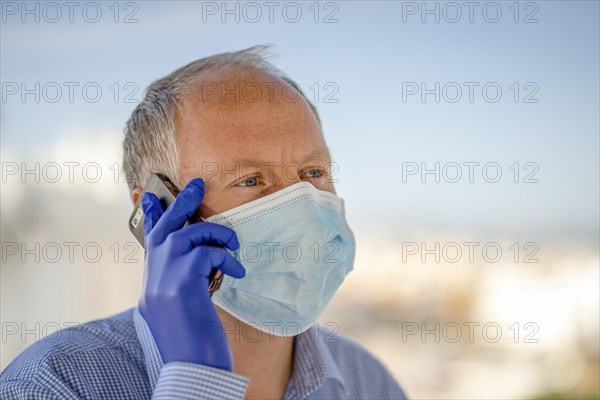 Man with protective mask and blue latex gloves while using mobile phone