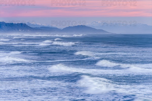 Leaking waves of the ocean under a pink evening sky with mountain silhouette, Punakaiki
