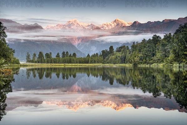 Veil clouds in front of Mount Cook and Mount Tasman are reflected in Lake Matheson in the evening light, Westland National Park