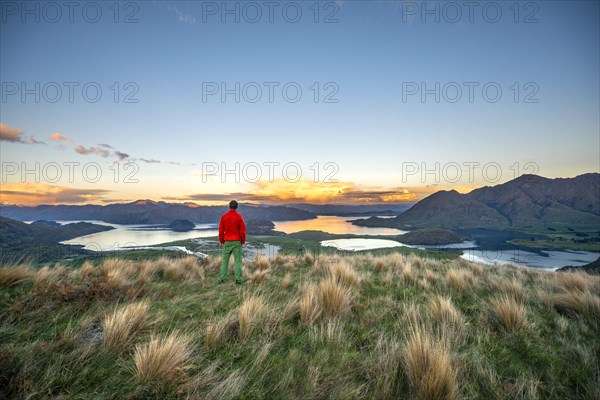 Walker looks out over Wanaka Lake and mountains at sunset, Rocky Peak